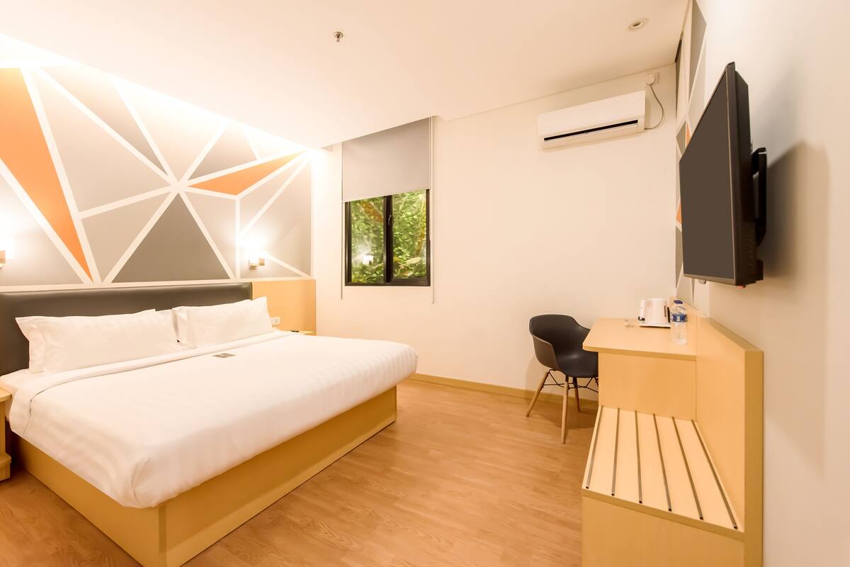 Een moderne hotelkamer met een bed, een bureau, een stoel, een televisie en een airconditioner.