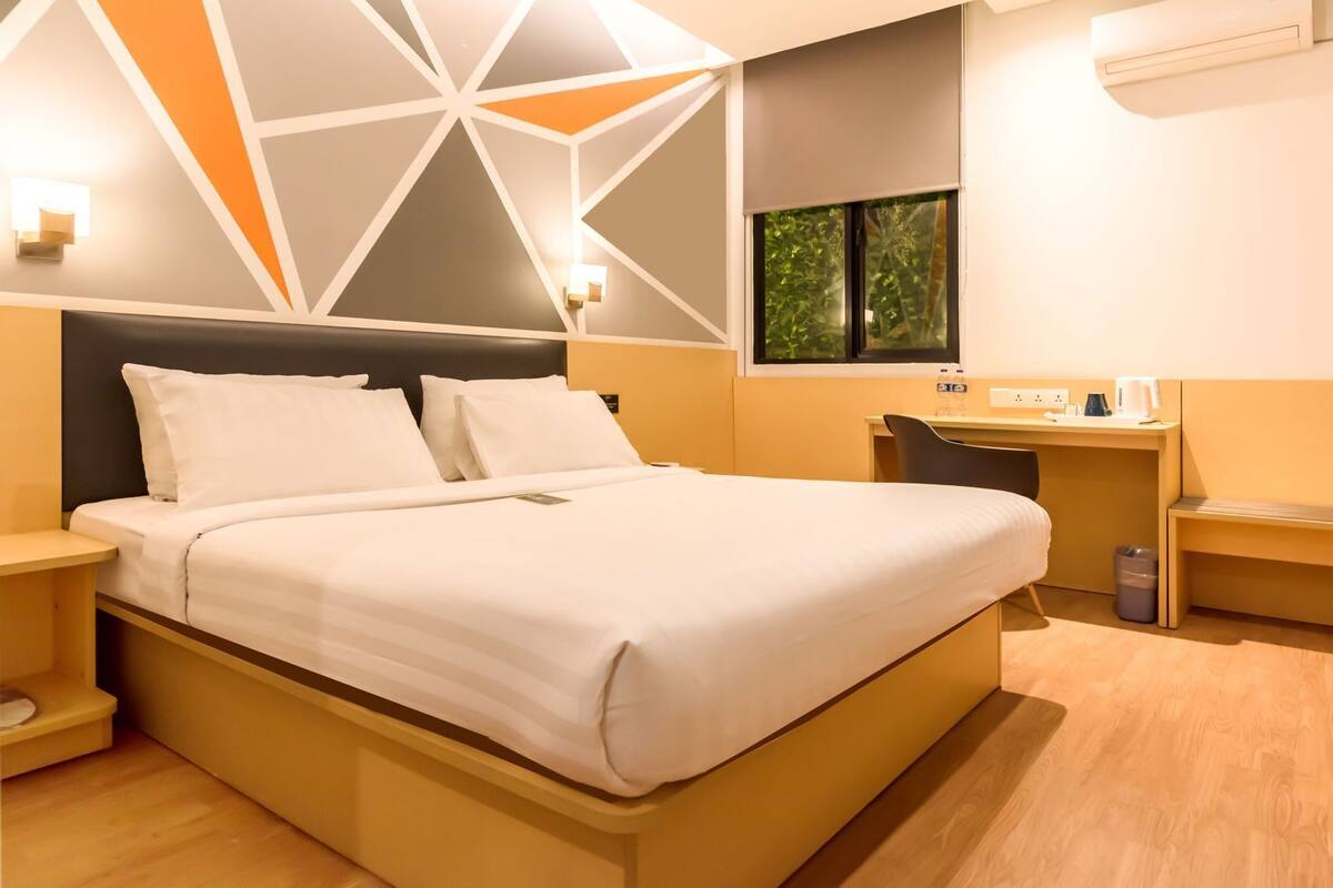 Een moderne hotelkamer met een bed, nachtkastjes, een bureau en een raam met uitzicht op groen.