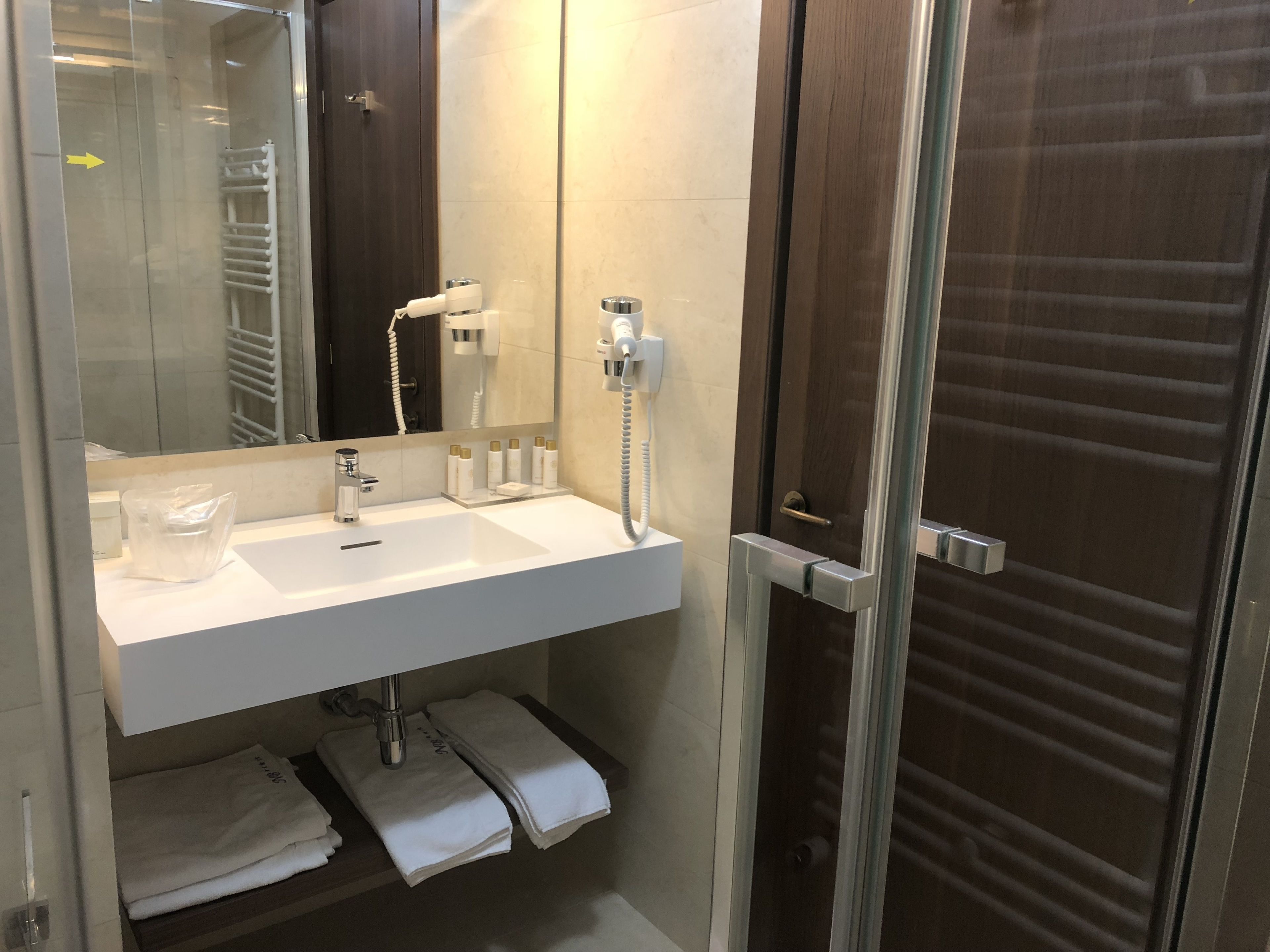 Een moderne badkamer met een wit wastafelmeubel, een spiegel, een handdoekrek en een douchehoek.