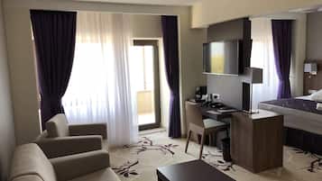 Una habitación de hotel con sofá, escritorio, computadora, televisor y cama.