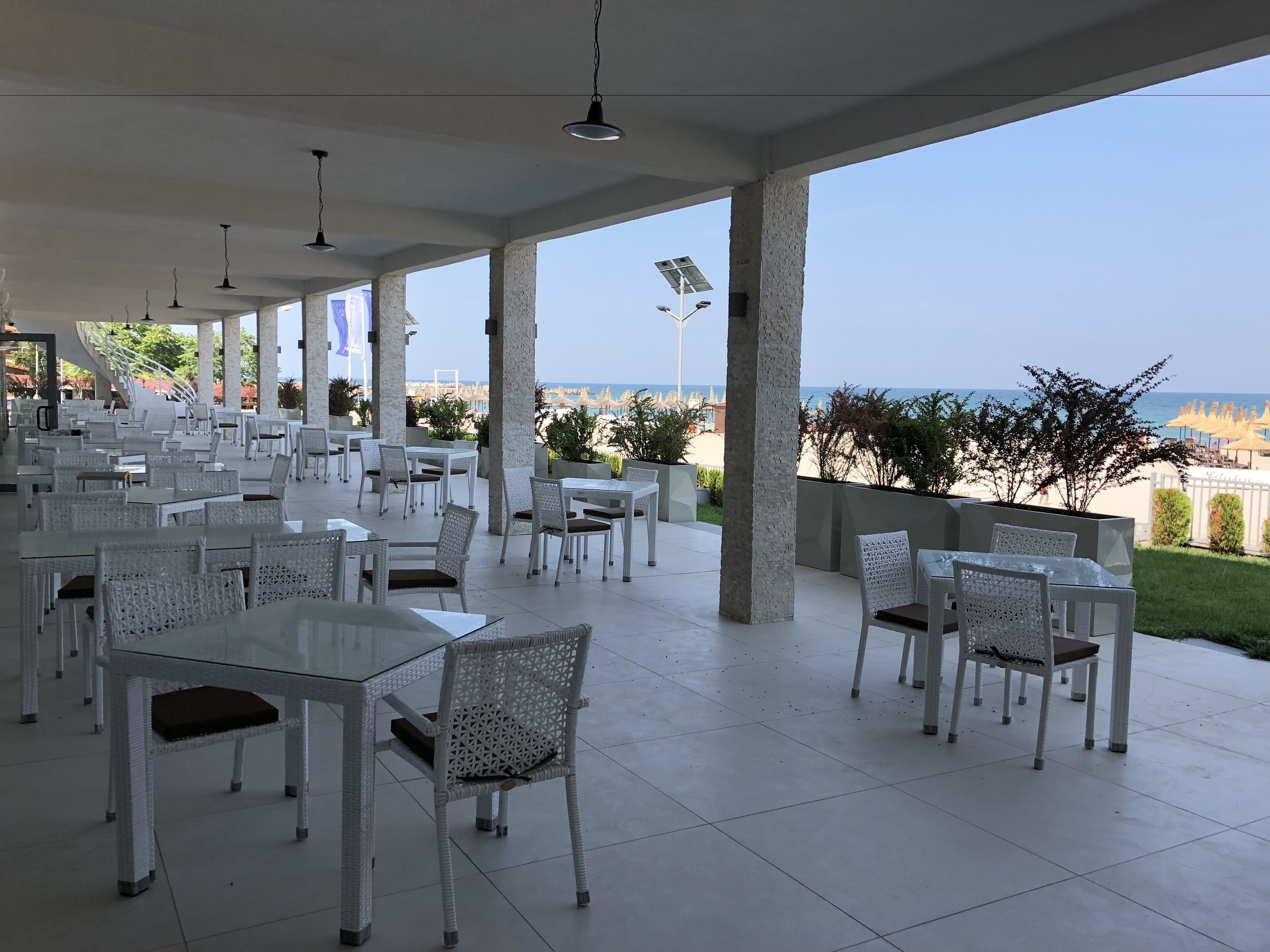 An outdoor dining area with white wicker furniture and a view of the beach.