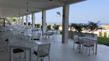 An outdoor dining area with white wicker furniture and a view of the beach.