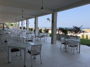 Un espace extérieur aménagé pour les repas, avec des meubles en osier blanc et une vue sur la plage.