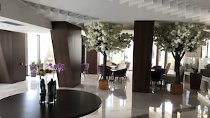 A modern lobby with a round table, purple chairs, and decorative trees with white flowers. - Hotel New Belvedere (Mangalia)