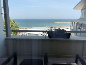 Un balcon avec des fauteuils en osier, une plante en pot et une vue sur la mer et la plage.