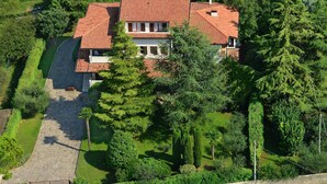 A large house with a red-tiled roof, surrounded by lush greenery and trees.