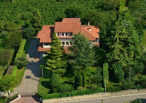 Vista aérea de una casa con techo de tejas rojas, rodeada de abundante vegetación y un jardín bien cuidado.