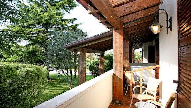 A balcony with wooden beams, a white railing, and a view of a well-maintained garden with trees and shrubs.