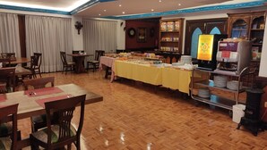 A dining area with wooden flooring, tables with chairs, a buffet table with food items, and a coffee machine. - Hotel Julia (Aranda de Duero)