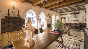 A dining area with a wooden table, chairs, and a statue. There are arched windows and a tiled floor. - Hotel Julia (Aranda de Duero)