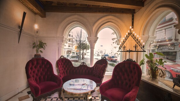 A room with three red velvet armchairs around a small round table, a chandelier, and a view of the street through arched windows. - Hotel Julia (Aranda de Duero)