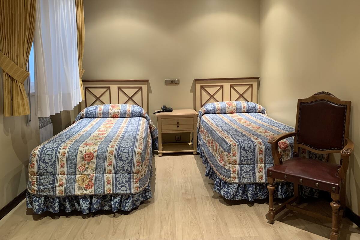 Una habitación con dos camas, una silla de madera y una mesita de noche.