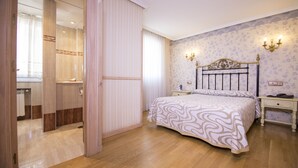 A bedroom with a bed, bedside tables, a nightstand, a mirror, and a wardrobe. - Hotel Julia (Aranda de Duero)