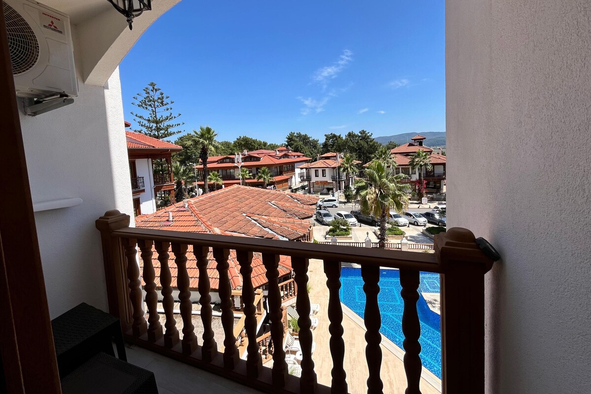 A balcony with a view of a swimming pool, red-roofed buildings, and palm trees.