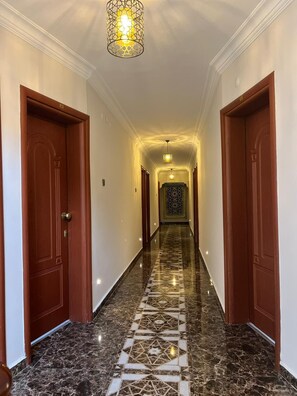 A hallway with marble flooring, wooden doors, and a patterned wall.