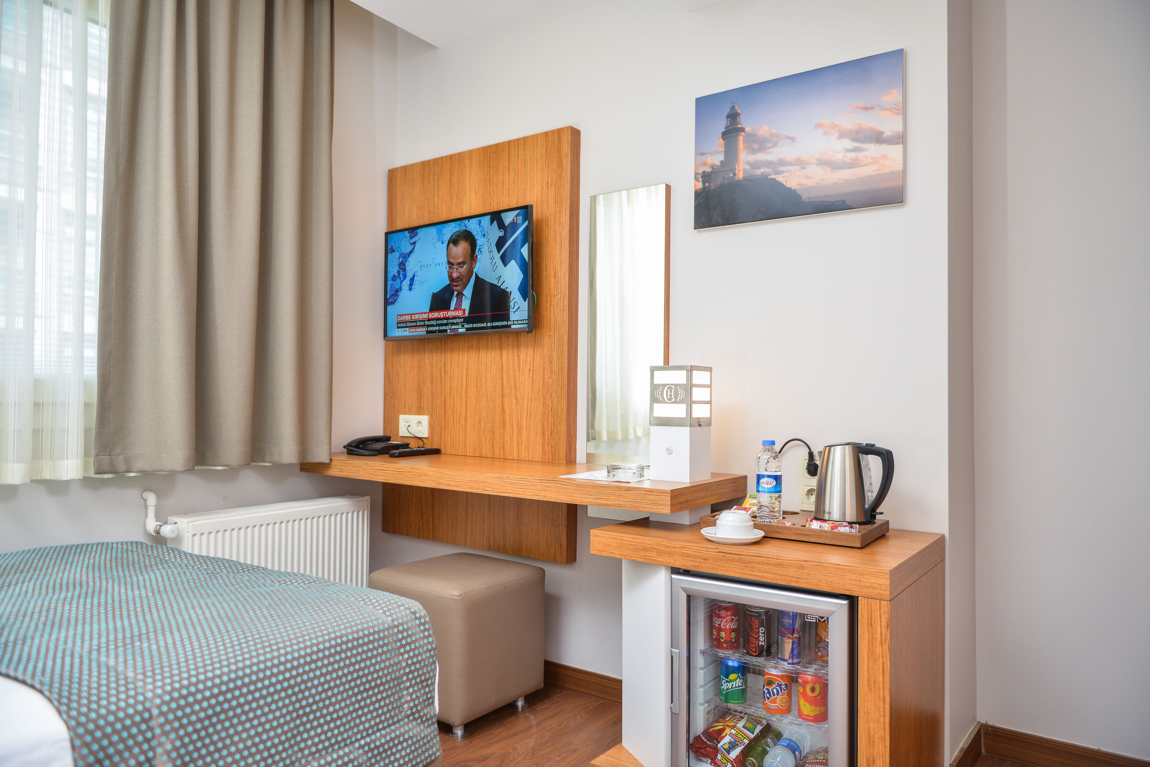 Una habitación de hotel con televisión, un refrigerador con bebidas, una cama y una ventana con cortinas.