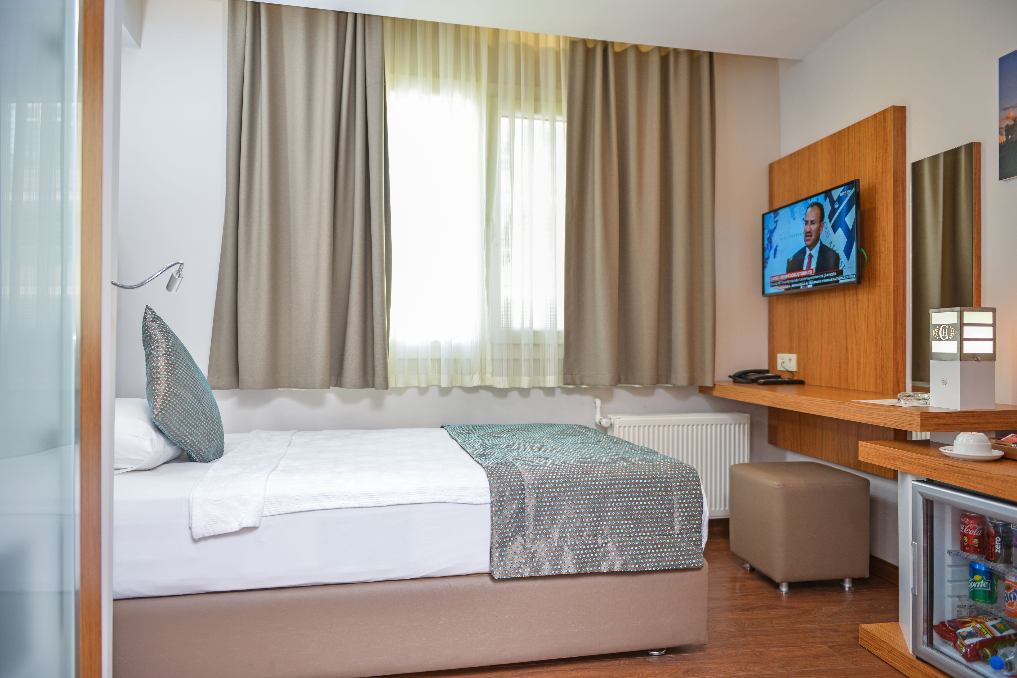 Una habitación de hotel con una cama, televisor, escritorio y refrigerador.