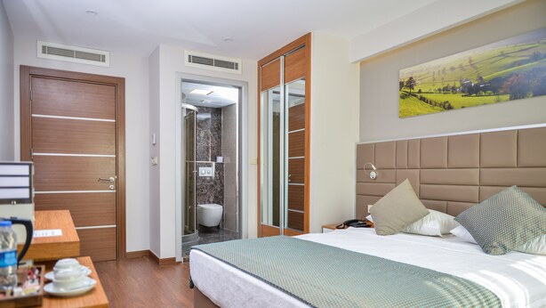 A hotel room with a bed, bedside table, and a painting on the wall. - Hakcan Hotel (Izmir)