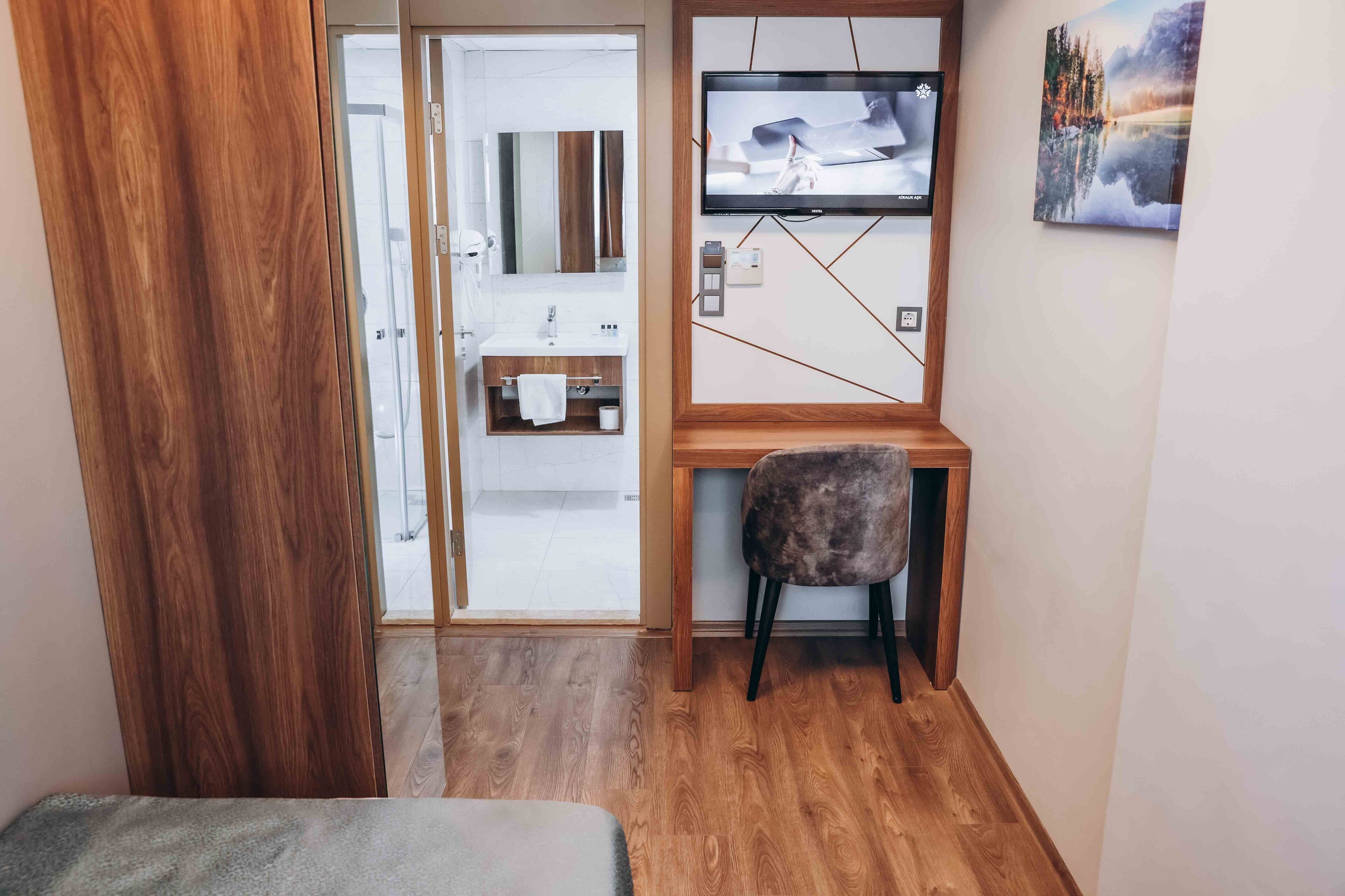 A compact room with a wooden desk, a chair, a small sofa, and a bathroom visible through a glass door.