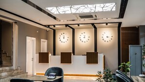 A modern reception area with three large wall clocks, a staircase, and a seating area with chairs and a table. - Hakcan Hotel (Izmir)