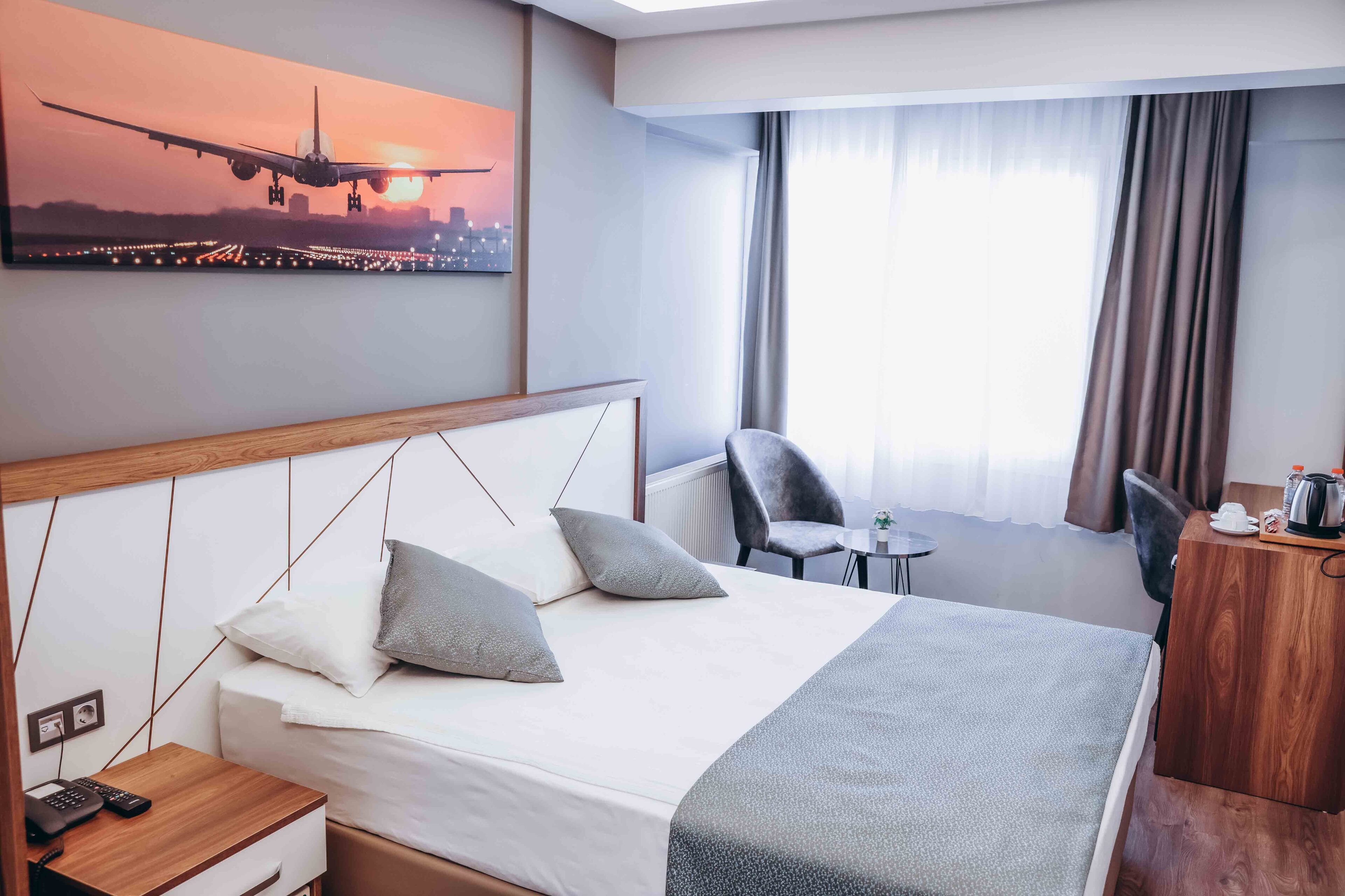 Une chambre d’hôtel comprenant un lit, une table de chevet, un petit bureau, une chaise, une table basse et une grande fenêtre avec des rideaux.