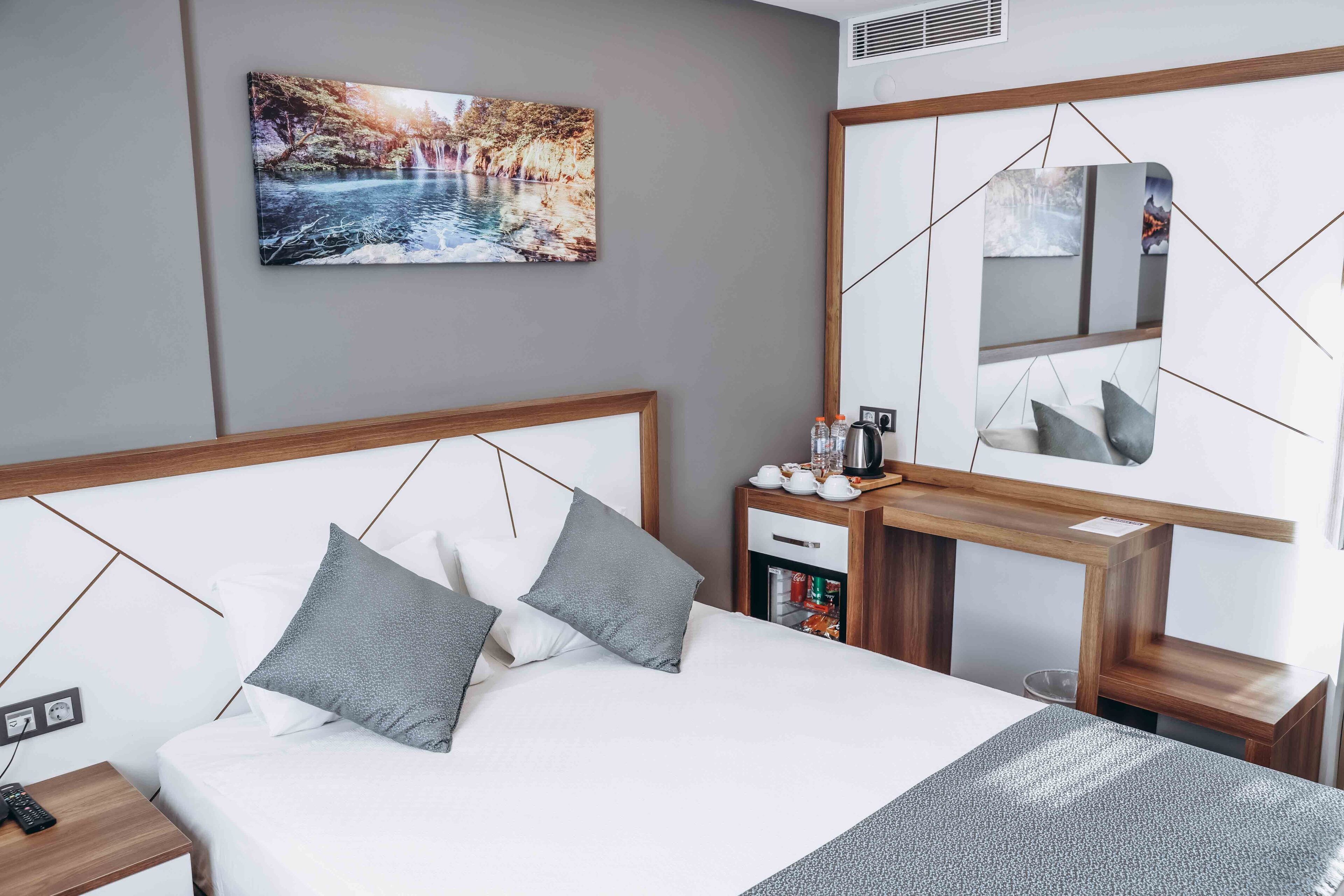 Een moderne hotelkamer met een groot bed, een nachtkastje met een waterkoker en een spiegel met geometrische patronen.
