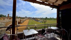 A balcony with tables and chairs overlooking a historical site with stone walls and a bridge. - Hostal Don Suero de Quiñones (Hospital de Orbigo)