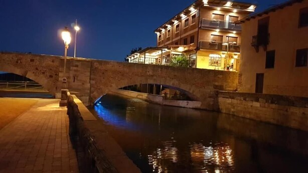 A stone bridge over a canal with a building on the right. - Hostal Don Suero de Quiñones (Hospital de Orbigo)