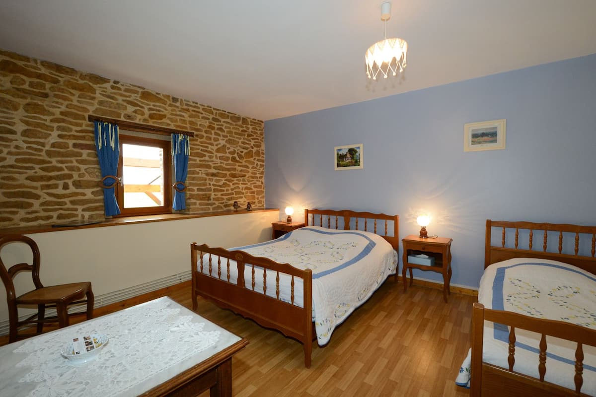 A bedroom with two wooden beds, a stone wall, a window with blue curtains, and a chandelier.