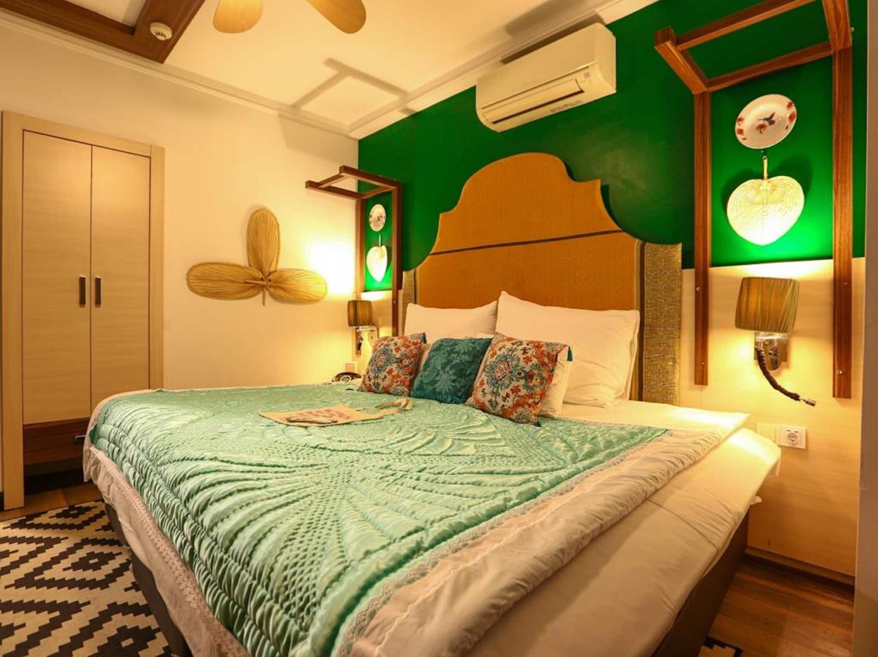 A bedroom with a large bed, a wooden wardrobe, a green accent wall, and a wall-mounted air conditioner.