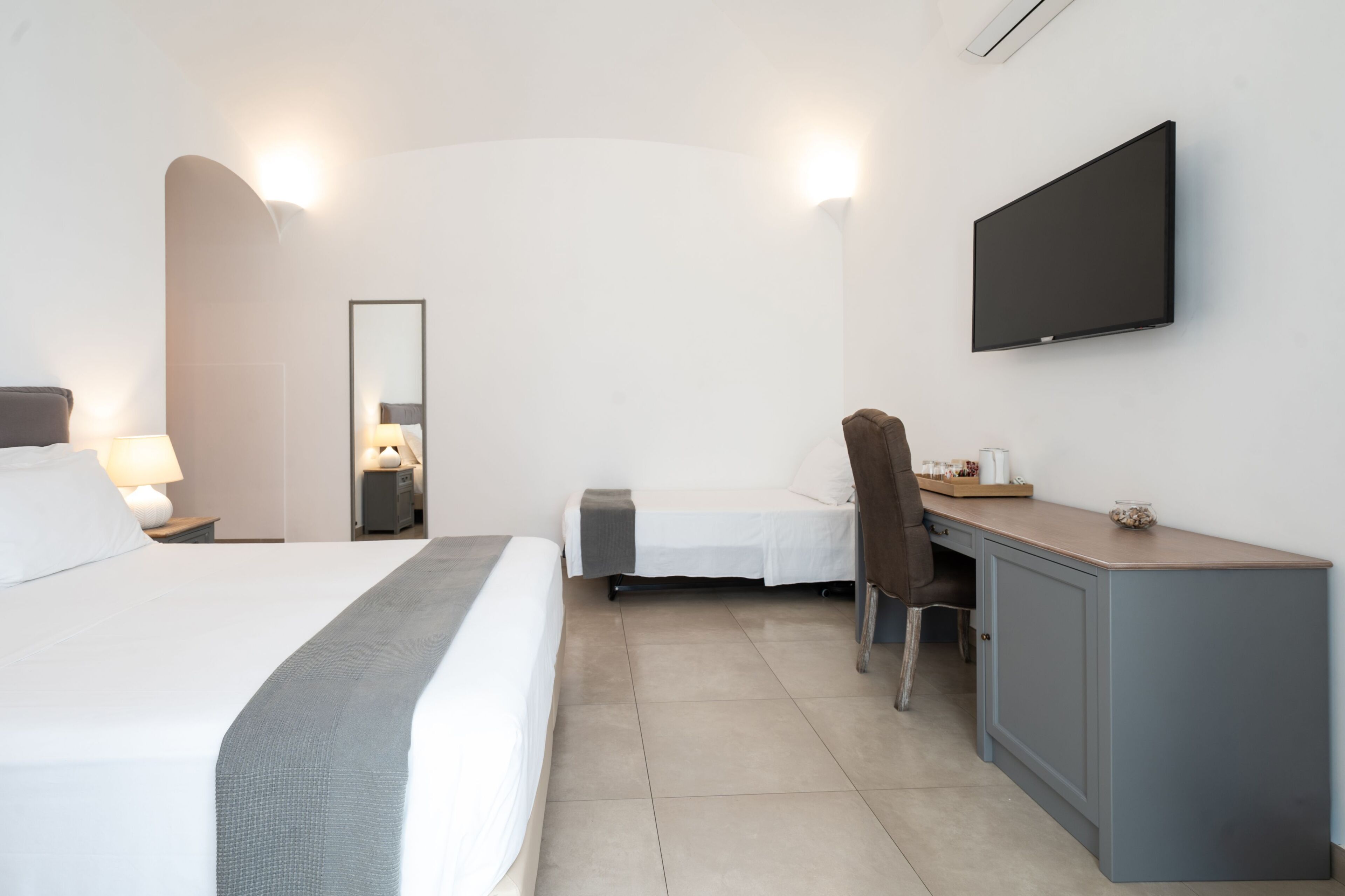 A hotel room with a large bed, a desk, a chair, a flat-screen TV, and a mirror.