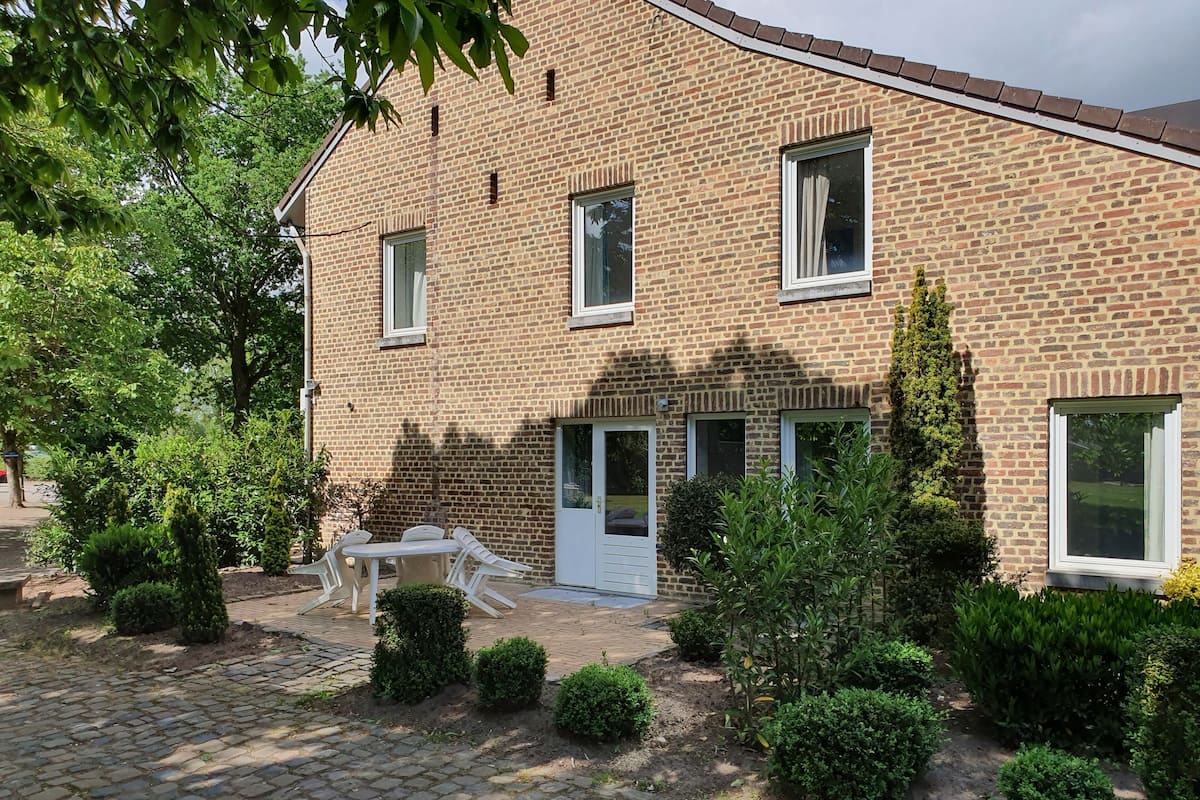 Een bakstenen huis met een verharde oprit, een witte deur en een klein terras met een tafel en stoelen.