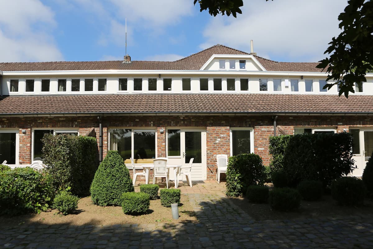 Een gebouw met twee verdiepingen, een betegeld dak, meerdere ramen en een terras met stoelen en plantenpotten.