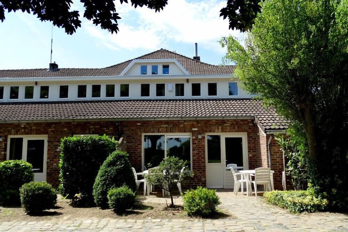 Een gebouw met twee verdiepingen, een pannendak, een bakstenen gevel en een klein terras met zitplaatsen.