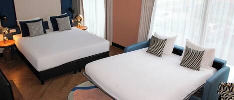A hotel room with two beds, a large window with sheer curtains, a blue armchair, and a round rug.