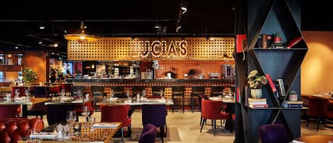 A modern restaurant interior with a bar area, multiple dining tables, and red and purple chairs.