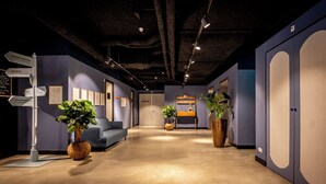 Un interior moderno con mostrador de recepción, señalización direccional, un sofá azul y plantas en macetas.