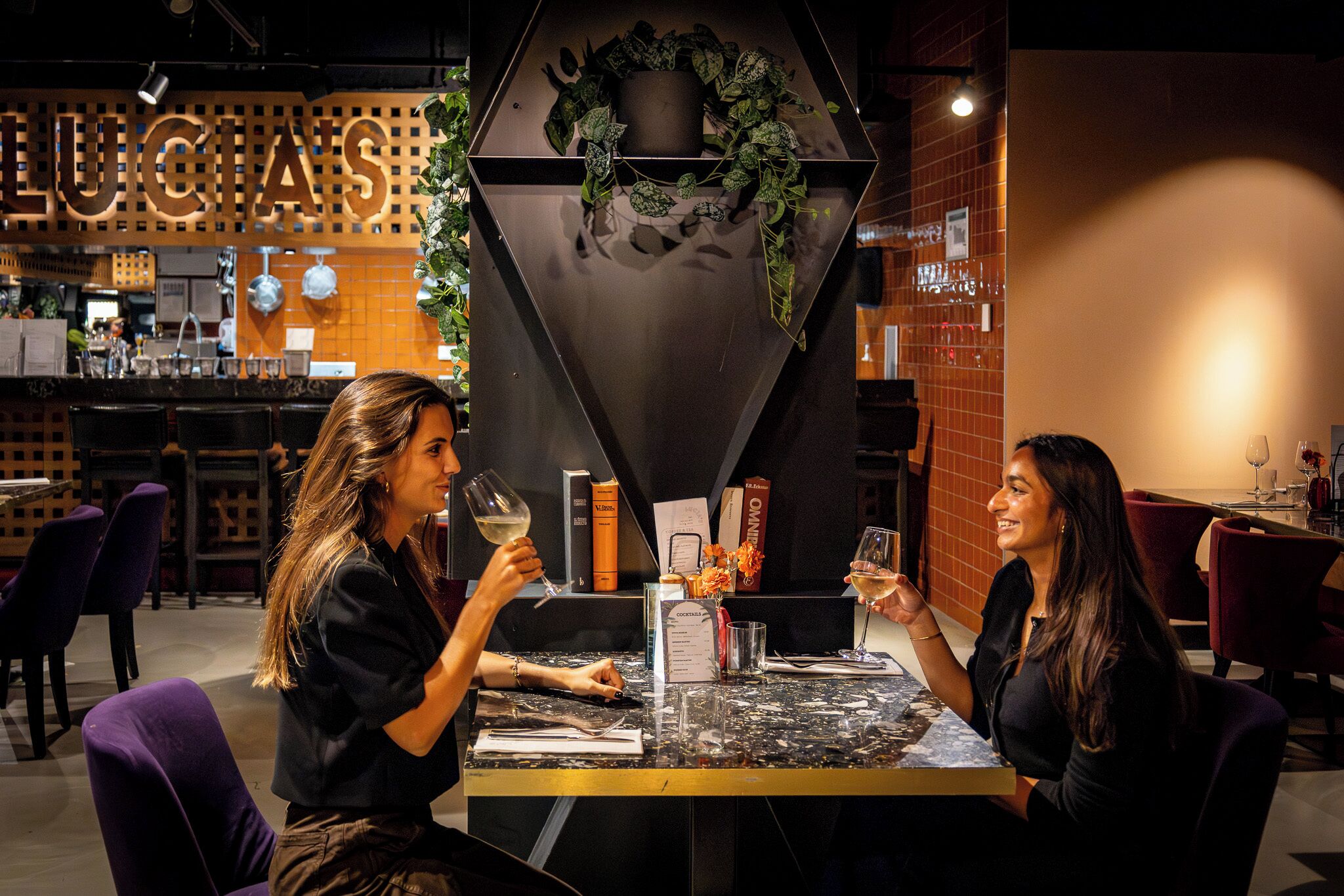Two people seated at a table in a restaurant with a modern interior, including a bar area in the background.