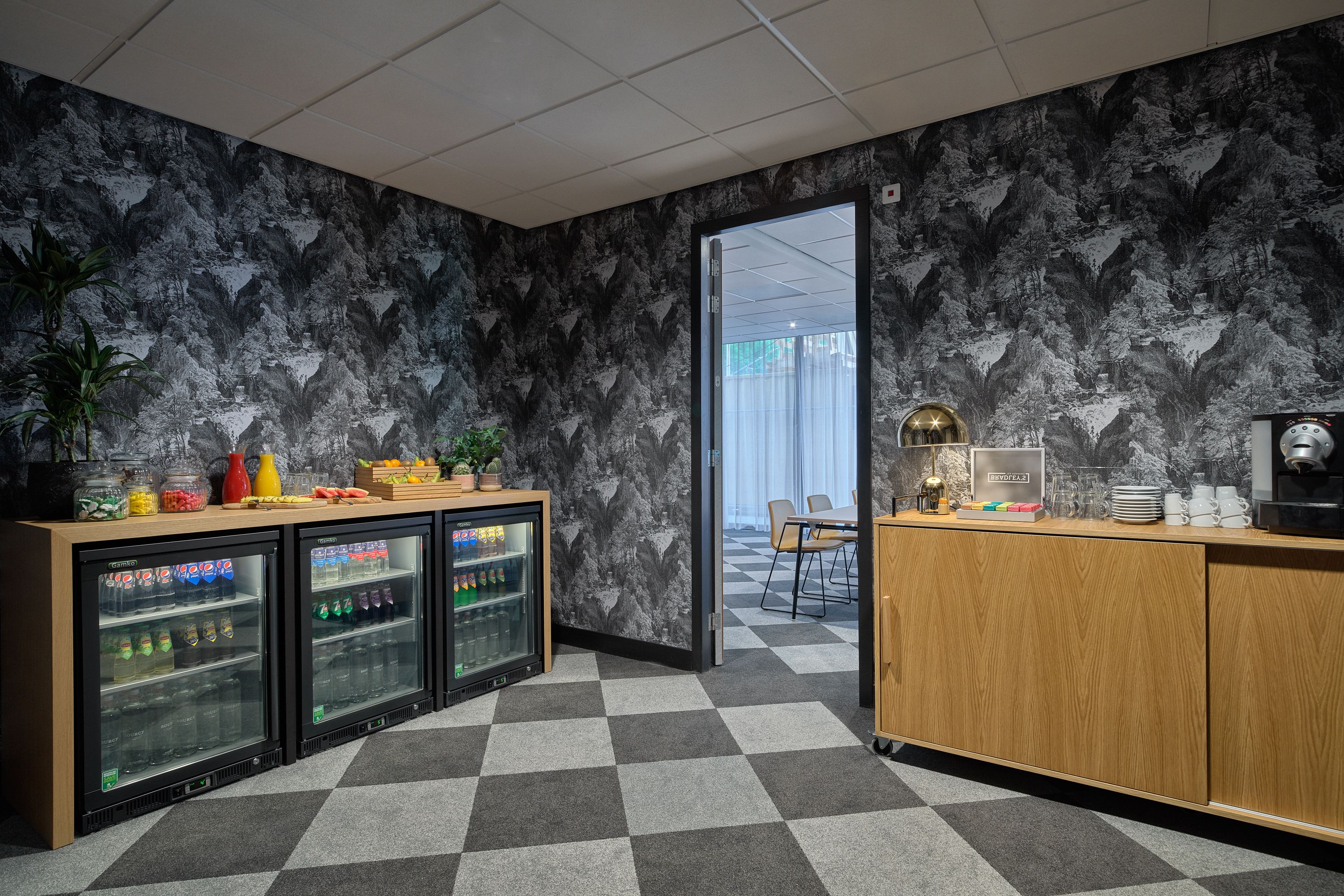 A modern kitchen area with a checkered floor, a refrigerator with beverages, a wooden cabinet, and a view into another room.