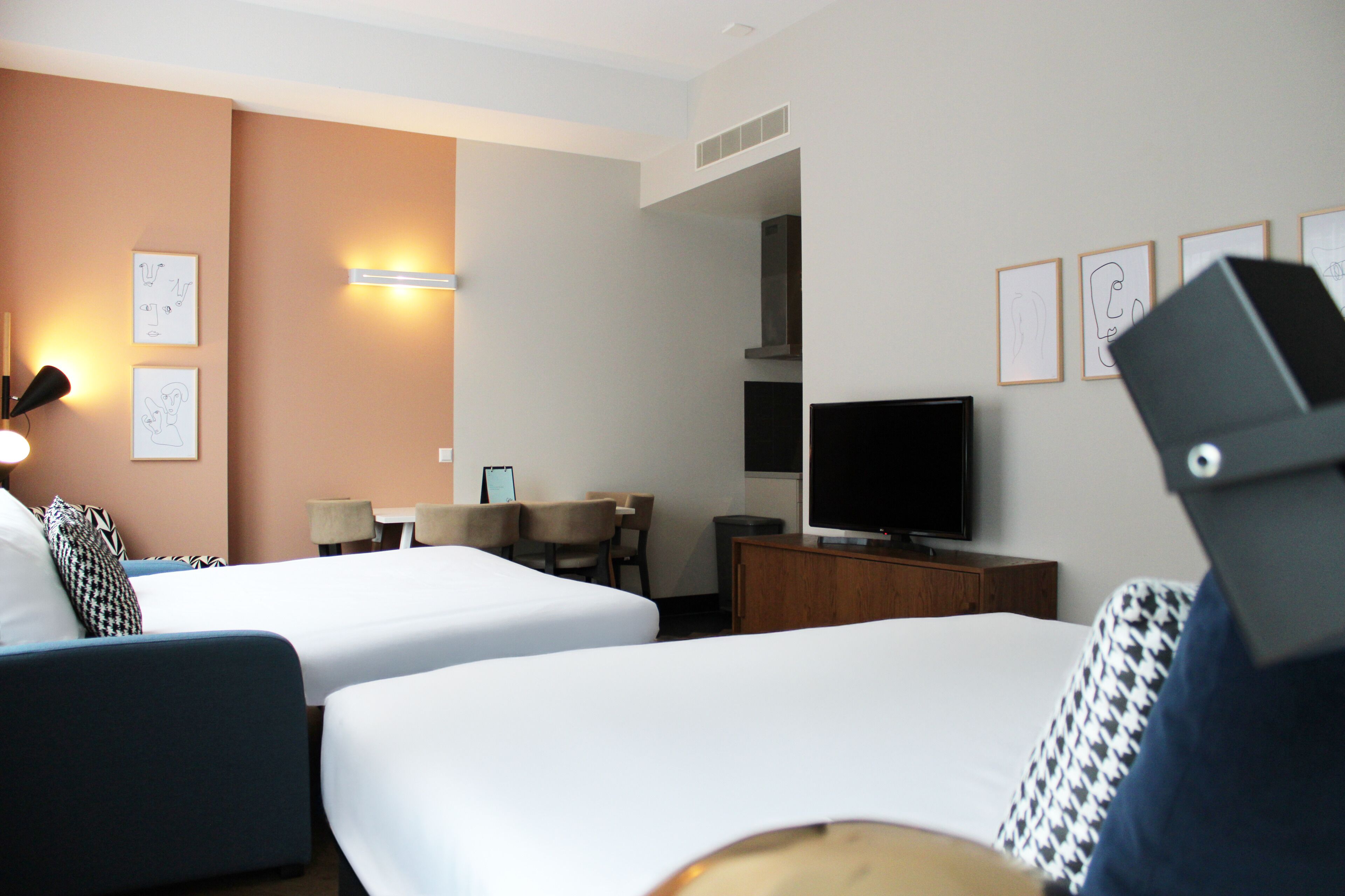 A hotel room with two beds, a desk, a chair, a television, and artwork on the walls.