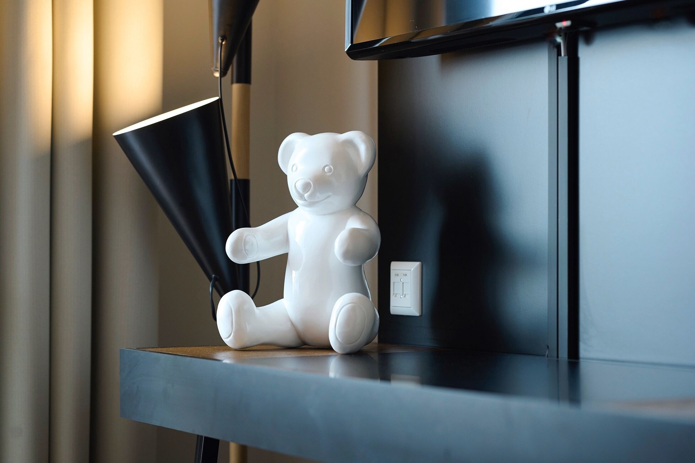 Une figurine d’ours en céramique blanche, posée sur une étagère, à côté d’une lampe noire.