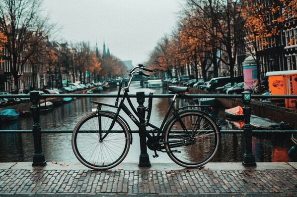 Una bicicleta aparcada junto a un canal, con un puente al fondo.