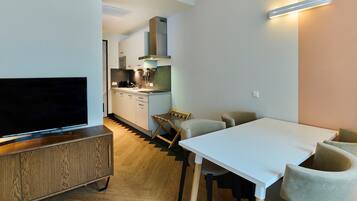 Une cuisine moderne dotée d’une cuisinière intégrée, d’un coin repas avec une table et des chaises blanches, et d’un téléviseur posé sur un meuble en bois.