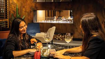 Deux personnes sont assises à une table, devant des bougies et un vase de fleurs.