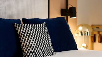A bed with blue and houndstooth patterned pillows, a wall-mounted light, and a partial view of a wooden shelf.
