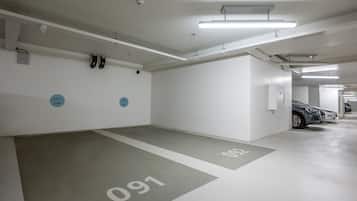 Un parking propre et moderne, avec des murs et des sols blancs, des places de stationnement clairement délimitées et un éclairage fluorescent au plafond.