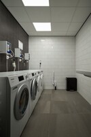Un moderno cuarto de lavandería con varias lavadoras, un contenedor de basura y un calentador de agua.