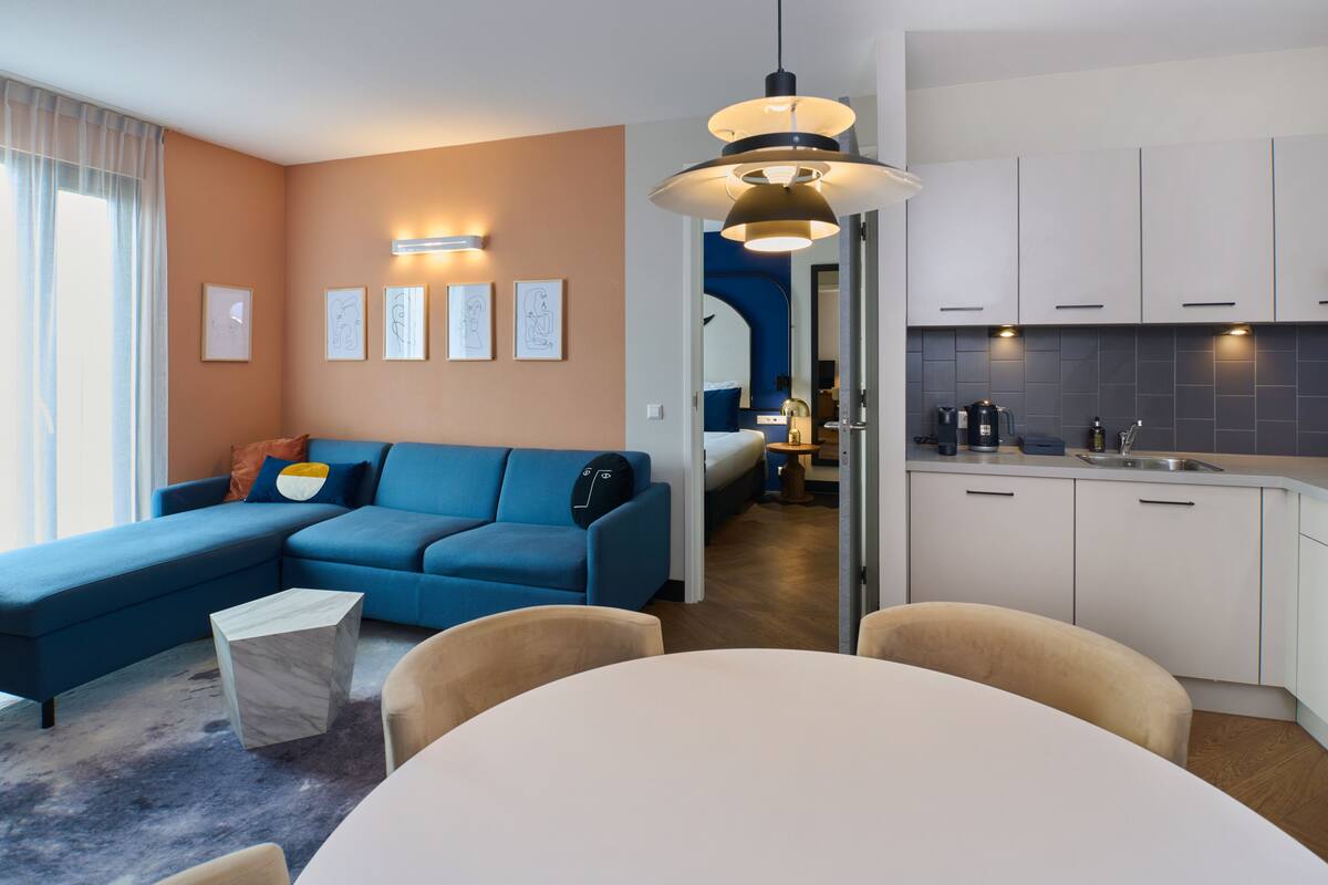 Una sala de estar moderna con un sofá azul, una mesa de centro de mármol y un comedor con una mesa y sillas blancas.