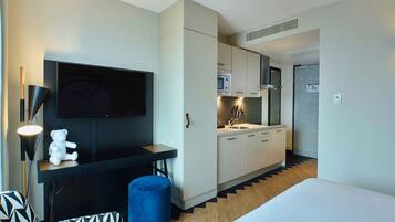 A compact hotel room with a kitchenette, a flat-screen TV, a small seating area, and a bed.