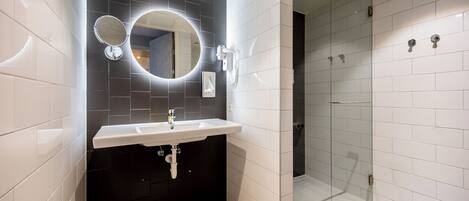A modern bathroom with a white sink, a round mirror, and a glass-enclosed shower.